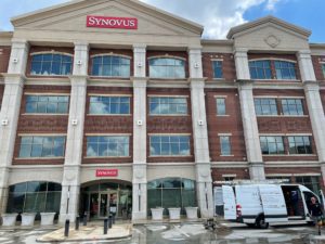 A large brick and stone building with "SYNOVUS" signage stands under a cloudy sky, with a white van parked in front.